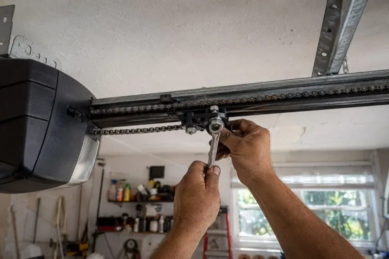Hands holding a wrench against an opener trolley beneath a chain rail — Chain-Drive Opener Repair, New Tecumseth