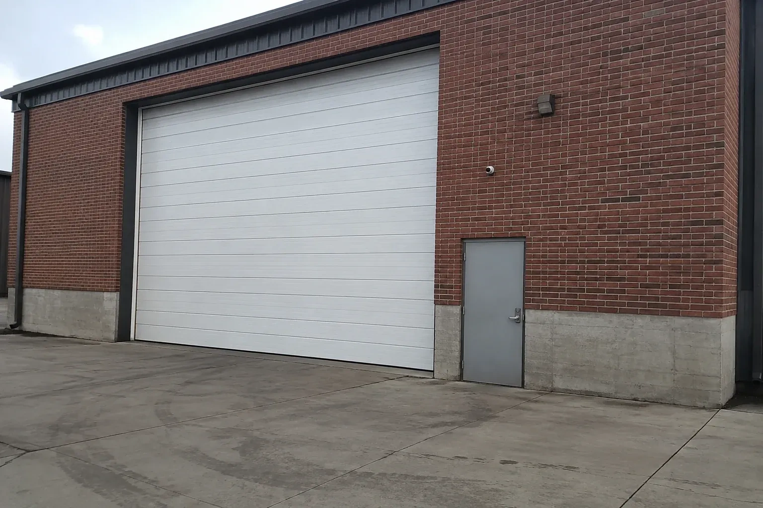 Tall closed sectional loading door beside a personnel door at a brick unit. — Commercial Sectional Door Repair, New Tecumseth