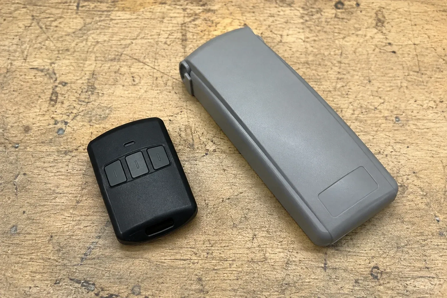 Three-button remote beside a closed grey keypad cover on a workbench. — Garage Door Remote and Keypad Programming, New Tecumseth